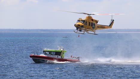 RAC-Rescue-Helicopter-Lifting-Up-And-Away-From-Marine-Rescue-Boat-During-Training,-handheld-clip