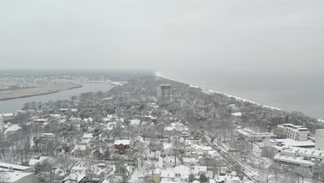 Drohnenaufnahme-Des-Verschneiten-Jurmala-Aus-Der-Luft,-Im-Hintergrund-Sieht-Man-Die-Ostsee-Und-Babītes-Ezers