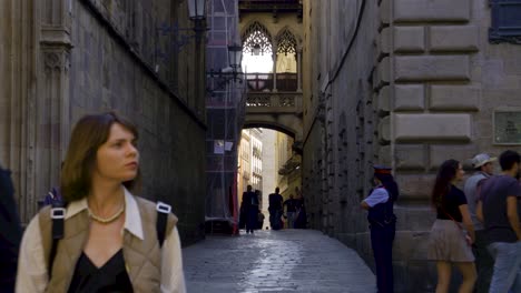 Pont-del-Bisbe,-Barcelona,-with-couple-and-tourists-walking-through-narrow-street-in-Barri-Gothic-Quarter