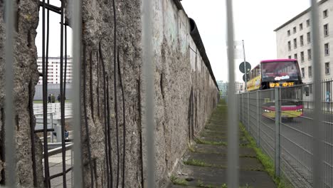 Blick-Entlang-Eines-Abschnitts-Der-Ursprünglichen-Berliner-Mauer-Auf-Die-Topographie-Des-Terrors-In-Berlin-Durch-Einen-Drahtzaun-Und-Einen-Sich-Nähernden-Touristenbus