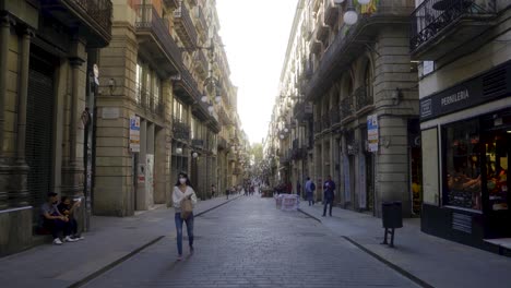 Forward-shot-through-long-central-street-in-Barri-Gothic-quarter-of-Barcelona-with-people-starting-their-day-in-the-morning-and-walking-over-pavement