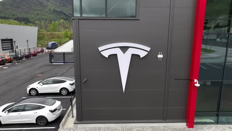 Tesla-Electric-Cars-Logo-Auf-Dem-Gebäude-Ihres-Autohauses-In-Forde,-Norwegen-–-Von-Der-Logo-Nahaufnahme-Bis-Hin-Zur-Langsamen-Rückwärtsbewegung,-Die-Das-Gebäude-Und-Die-Tesla-Autos-Enthüllt