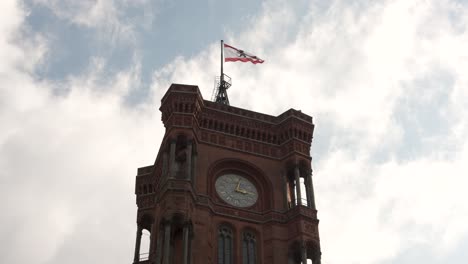 Looking-Up-At-Rotes-Rathaus-Clock-Tower-With-Flag-Of-Berlin-Fluttering-In-Wind