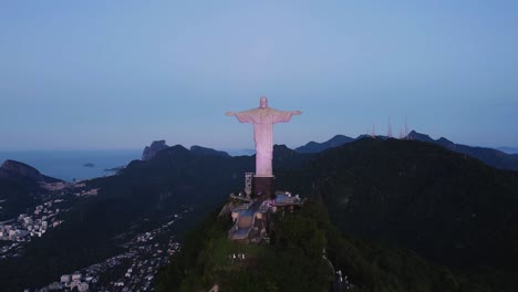 Aerial-view-approaching-the-illuminated-Christ-the-Redeemer-statue,-dusk-in-Rio-de-Janeiro,-Brazil
