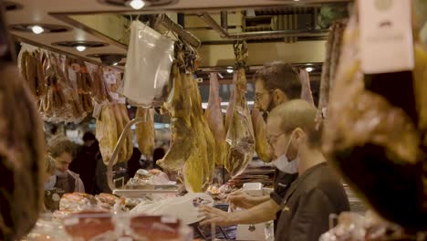 Vendors-of-butcher-shop-taking-payment-of-food-and-produce-at-Mercado-de-La-Boqueria-in-Barcelona,-Spain-in-the-evening