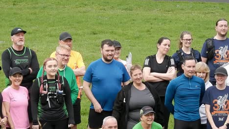 Group-of-community-runners-gathered-talking-and-supporting-each-other-in-local-park-field-at-start-of-their-fitness-run