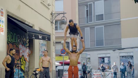 Street-performers-performing-spectacular-athletic-tricks-during-live-street-show-in-front-of-crowd-of-tourists-sitting-at-bars-and-restaurants-in-Barcelona,-Spain-during-sunset-on-warm-evening