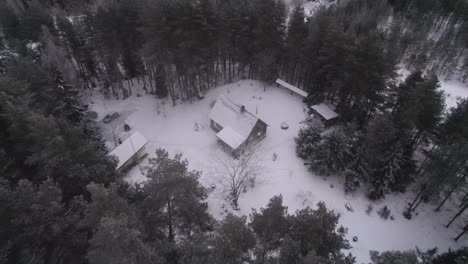 Drohnenaufnahme-Des-Herauszoomens-Aus-Einem-Verschneiten-Haus-Mitten-In-Einem-Großen-Wald