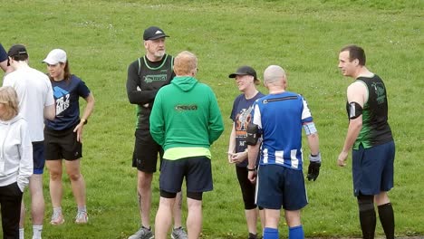 Group-of-runners-gathered-talking-and-supporting-each-other-in-local-park-field-at-beginning-of-their-fitness-run