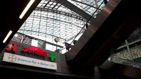 Rotes-Schild-Der-Apotheke-An-Der-Wand-Im-Berliner-Hauptbahnhof-Mit-Silbernen-Mehrstufigen-Rolltreppen