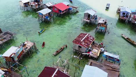 Slow-aerial-flyover-shot-of-water-houses-and-fishermen-with-boats-in-crystal-clear-sea-water-at-Pulau-Omodal-Semporna,-Sabah,-Malaysia