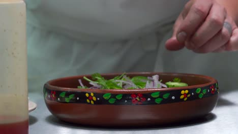 Mexican-chef-adding-chilli-and-hot-sauce-salsa-on-top-of-sausage-dish-with-red-onion-coriander-salad