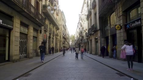 Forward-shot-through-long-central-street-in-Barri-Gothic-quarter-of-Barcelona-with-people-starting-their-day-in-the-morning-and-walking-over-pavement