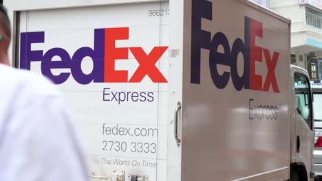 Chinesische-Fußgänger-Gehen-An-Einem-FedEx-Lastwagen-Des-Amerikanischen-Lieferservices-Und-Logistikunternehmens-Vorbei,-Der-Auf-Der-Straße-Von-Hongkong-Stationiert-Ist