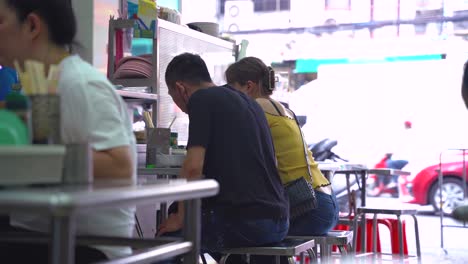 Shot-of-Two-Thaï-Persons-Eating-In-A-Thaï-Street-Food-Restaurant-in-Chinatown-During-the-Day,-Bangkok