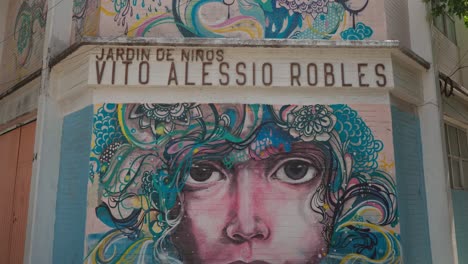 Graffiti-Con-Rostros-Y-Formas-Orgánicas-En-Tonos-Azules-Y-Amarillos-Pintados-En-La-Esquina-De-La-Escuela-Infantil-Vito-Alessio-Robles-En-El-Barrio-Roma,-Ciudad-De-México.