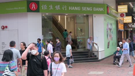 Los-Peatones-Pasan-Por-Delante-De-La-Empresa-De-Servicios-Bancarios-Y-Financieros-Con-Sede-En-Hong-Kong-Y-Del-Principal-Indicador-Del-Mercado-De-Valores-De-Hong-Kong,-Hang-Seng-Bank,-Sucursal-En-Hong-Kong