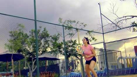 An-athletic-woman-playing-beach-tennis-jumps-up-to-hit-a-ball-with-her-racket
