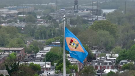 Bandera-De-Delaware-Ondeando-Frente-A-La-Ciudad,-Viviendas-Urbanas-En-Una-Mañana-Brumosa-Y-Nublada