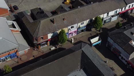 Aerial-view-above-small-town-market-street-retail-shops-and-supermarket-rooftops-during-recession,-Zoom-in-shot