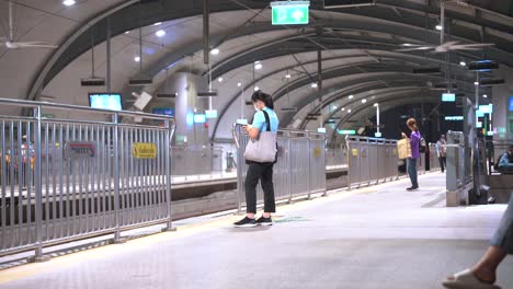 Mujer-Tailandesa-Esperando-El-Metro-En-La-Plataforma-BTS-De-Bangkok-Por-La-Noche-Con-Poca-Gente-Alrededor,-Tailandia