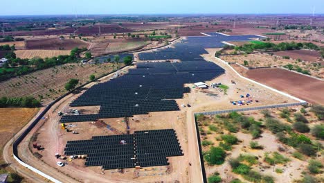 An-aerial-drone-camera-is-circling-where-a-whole-solar-pump-is-visible-in-the-distance,-generating-green-energy-and-delivering-it-to-a-nearby-power-station