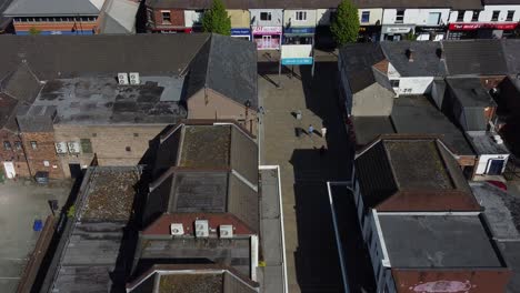 Aerial-view-zoom-in-over-people-in-small-town-market-high-street-retail-shops-and-supermarket-rooftops-during-inflation-crisis
