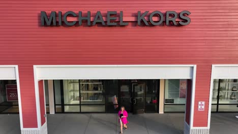 Aerial-rising-shot-of-Michael-Kors-store-with-rich-woman-walking-out-of-door