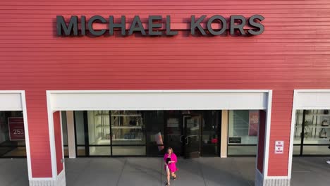 Toma-Aérea-En-Ascenso-De-La-Tienda-De-Michael-Kors-Con-Una-Mujer-Rica-Saliendo-Por-La-Puerta