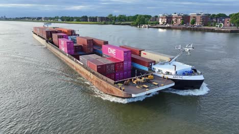 Aerial-View-Of-Arctic-Cargo-Container-Ship-Paired-With-Barge-Travelling-Along-River-Noord