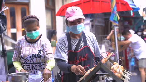Aufnahme-Von-Zwei-Thailändischen-Straßenverkäufern-Mit-Maske-In-Chinatown,-Die-Tagsüber-Schweinswurst-Verkaufen,-Bangkok