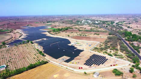 Extrem-Weite-Ansicht,-Bei-Der-Sich-Die-Drohnenkamera-Aus-Der-Luft-Um-Ein-Solarkraftwerk-Dreht,-Das-Grüne-Energie-Produziert-Und-An-Ein-Nahegelegenes-Kraftwerk-Liefert