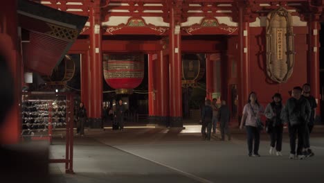 Grupo-De-Turistas-Asiáticos-Caminando-Por-La-Noche-A-Través-De-La-Puerta-Hozomon-Del-Templo-Sensō-ji-En-Asakusa,-Con-Tres-Linternas-Gigantes-Al-Fondo,-El-Templo-Budista-Más-Antiguo-De-Tokio,-Japón