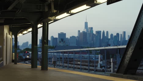 New-Yorker-U-Bahn-Auf-Hochbahn,-Die-In-Den-Bahnhof-Einfährt,-Mit-Der-Skyline-Von-Manhattan-Im-Hintergrund