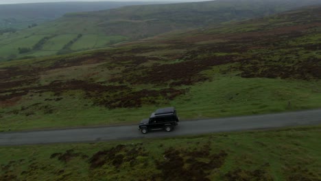 Black-Historic-Land-Rover-Defender-driving-down-winding-thin-single-lane-alongside-huge-green-valleys-and-hills-in-the-North-Yorkshire-Moors-near-Rosedale