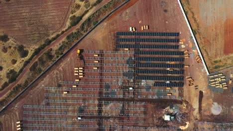 Vista-Aérea-De-Arriba-Hacia-Abajo-De-La-Instalación-De-Módulos-Solares,-Levantamiento-De-Cajas-Pesadas-Para-El-Proceso-De-Instalación-Y-Desembalaje-De-Módulos-Solares.