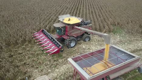 Tractor-Combine-Dumping-Corn-Into-Grain-Bin-While-Harvesting-In-Field-Aerial-Parallax-View