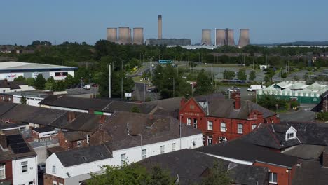 Aerial-view-descends-across-small-town-shops-rooftops-with-power-station-on-the-horizon-during-recession