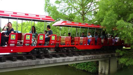 New-Orleans-USA-April-22nd-2023:-a-bright-red-train-car-is-moving-along-the-tracks-with-passengers-wavy-towards-the-camera-at-a-local-tourist-attraction-in-New-Orleans