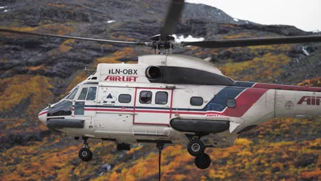 An-airlift-helicopter,-with-a-loading-cable-attached,-is-taking-off-from-the-landing-site-along-the-Trollstigen-mountain-road