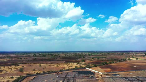 Aerial-camera-moving-down-above-the-solar-farm-grid,-beautiful-and-dramatic-clouds-background-at-agricultural-land-in-India