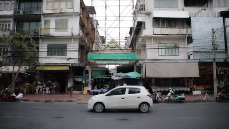 Entrada-Al-Mercado-De-Flores-Con-Vehículos-Pasando-Y-Gente-Cruzando-En-Bangkok