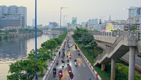 Aerial-view-of-riverside-motorbike-highway-with-river-view-and-building-on-the-background-in