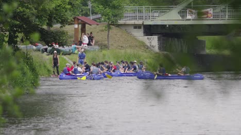 Eine-Gruppe-Bootsfahrer-Kommt-In-Mehreren-Booten-Am-Steinufer-Vor-Der-Brücke-An