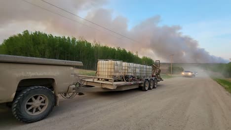 Truck-passby-carrying-wildfire-suppression-water-barrels-with-wildfire-smoke-in-sky,-Alberta,-Canada