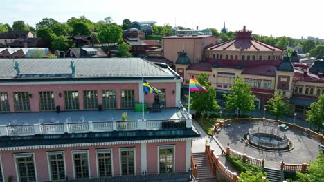 La-Bandera-Nacional-Sueca-Y-La-Bandera-Del-Arco-Iris-Del-Orgullo-Gay-Ondean-Juntas-En-Lo-Alto-Del-Edificio-Del-Hotel-En-El-Capitolio-De-Suecia,-Estocolmo---Hotel-Hasselbacken-En-Djurgarden