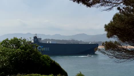 Wide-shot-of-UECC-Ship-entering-port-of-Santander-City-during-sunny-day---In-background-mountain-range-in-Spain