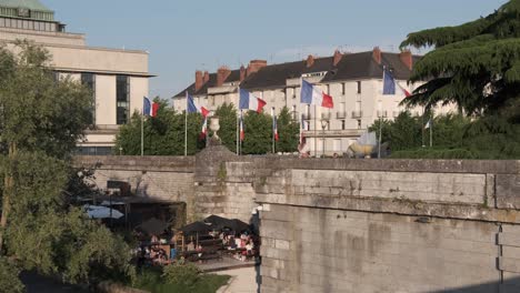 Public-library-French-flags-swinging-on-breeze,-with-people-below-the-walls-sitting-in-a-cafe,-life-on-street