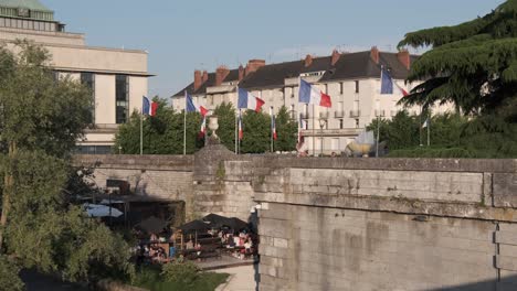 Biblioteca-Pública-Banderas-Francesas-Ondeando-Con-La-Brisa,-Con-Gente-Debajo-De-Las-Paredes-Sentada-En-Un-Café,-Vida-En-La-Calle