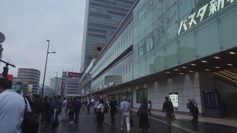 Commuters-Walking-Past-Outside-Shinjuku-Station-On-Dark-Overcast-Day-In-Tokyo